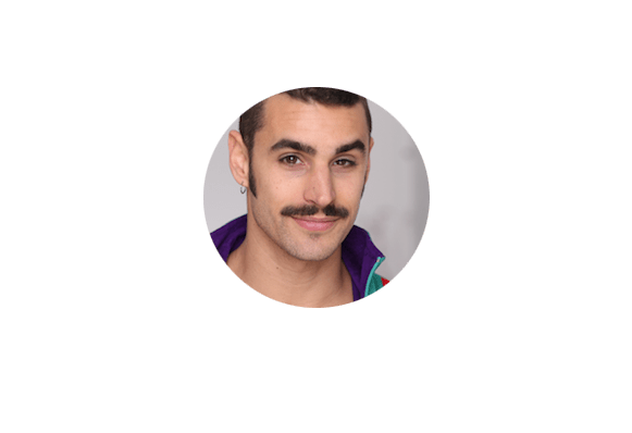 Un homme souriant avec une moustache, portant une veste colorée avec des touches de violet et de rouge.